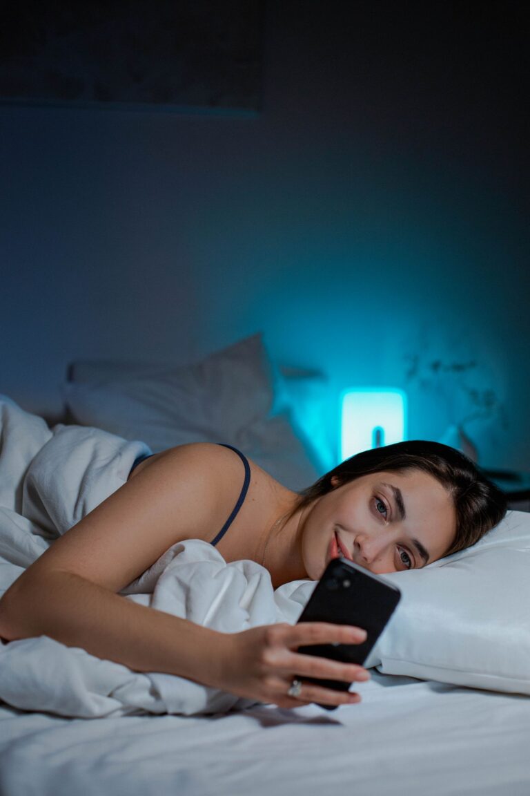 Nő az ágyban éjszaka, a telefon fénye világítja meg az arcát