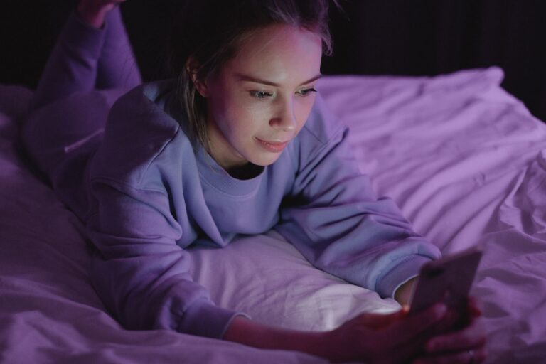 Nő az ágyban esti fényben, a telefonján chatel