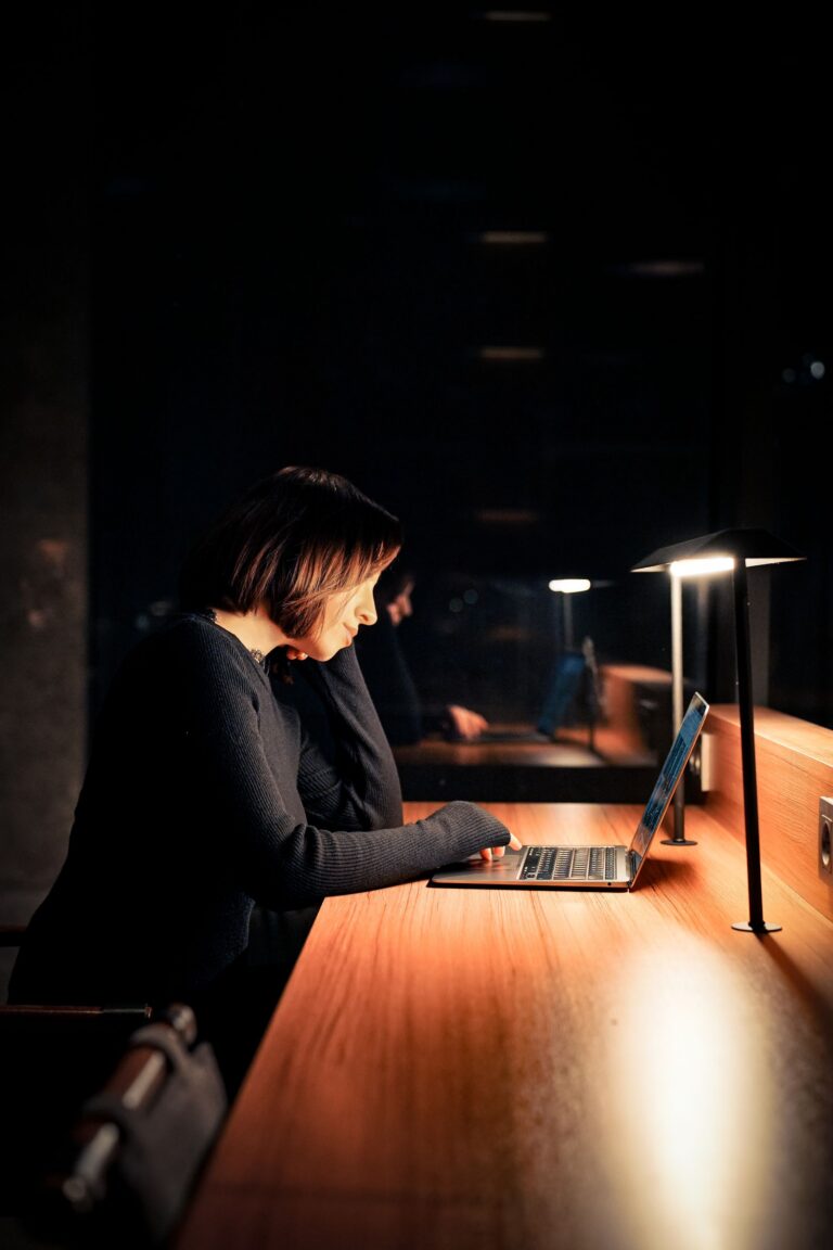 Nő egyedül a laptopja előtt, lámpafényben, este