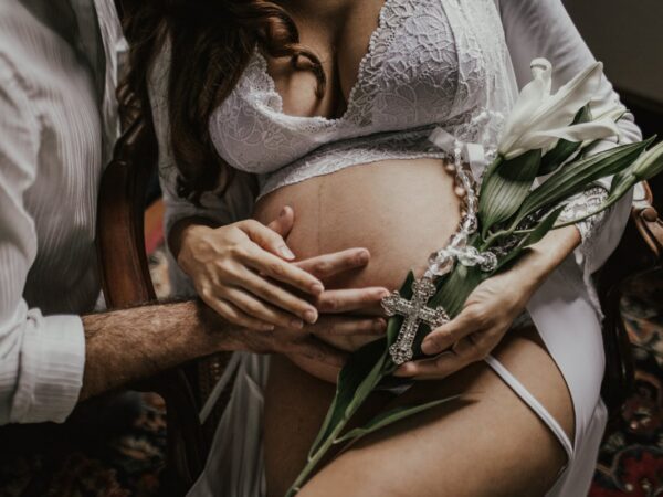 Terhes nő fehérneműben, partner öleli a hasát - szex terhesség alatt