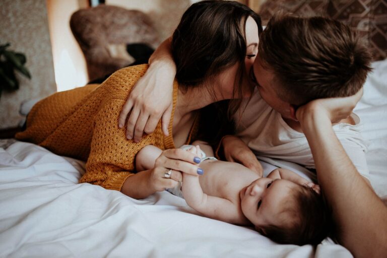 Fiatal szülők csókolóznak az ágyon, mellettük a kisbabájuk